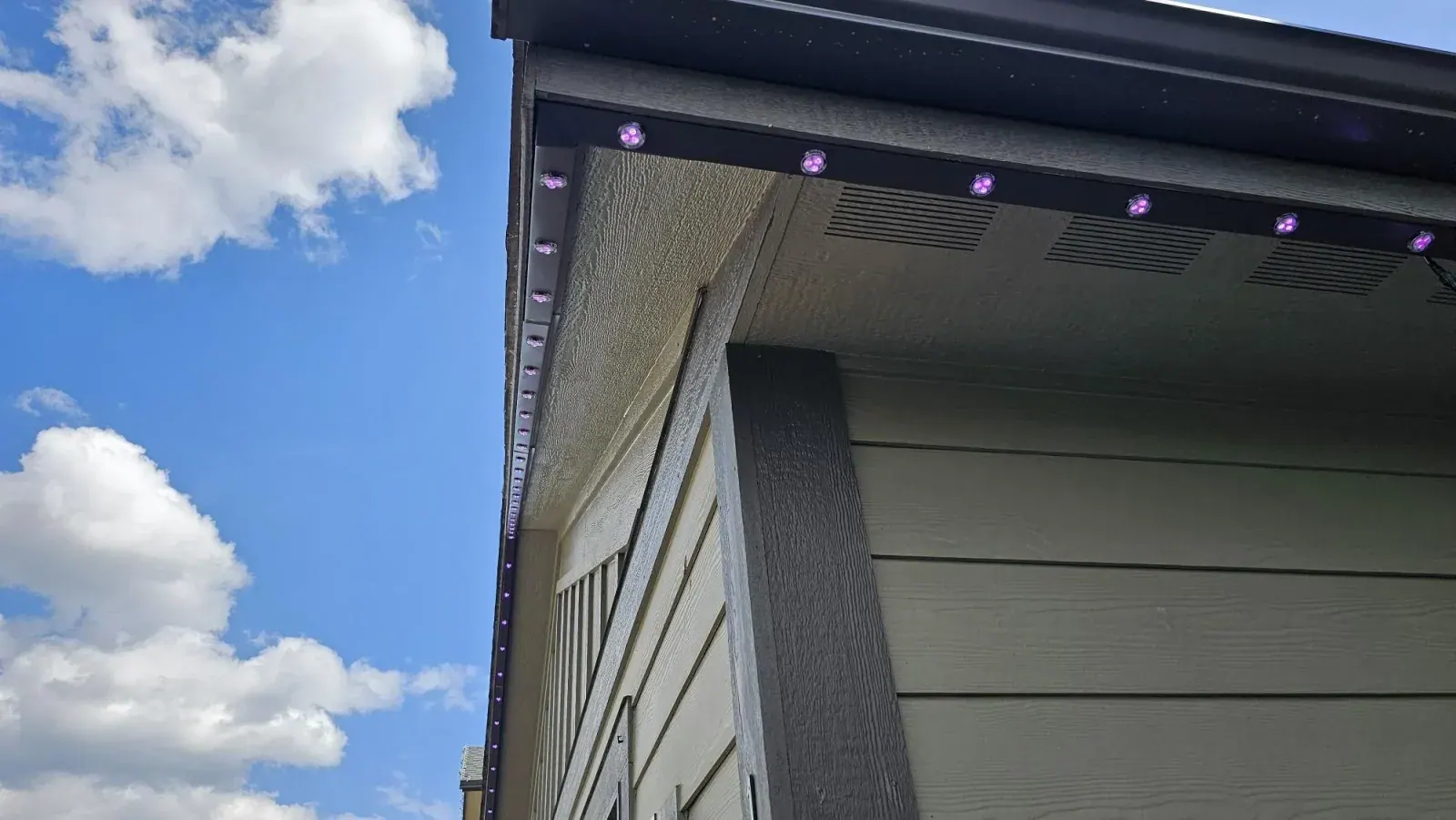 Close-up of a black aluminum permanent LED track with purple RGB light pucks mounted under an eave — permanent LED lighting near Exeter, Ontario